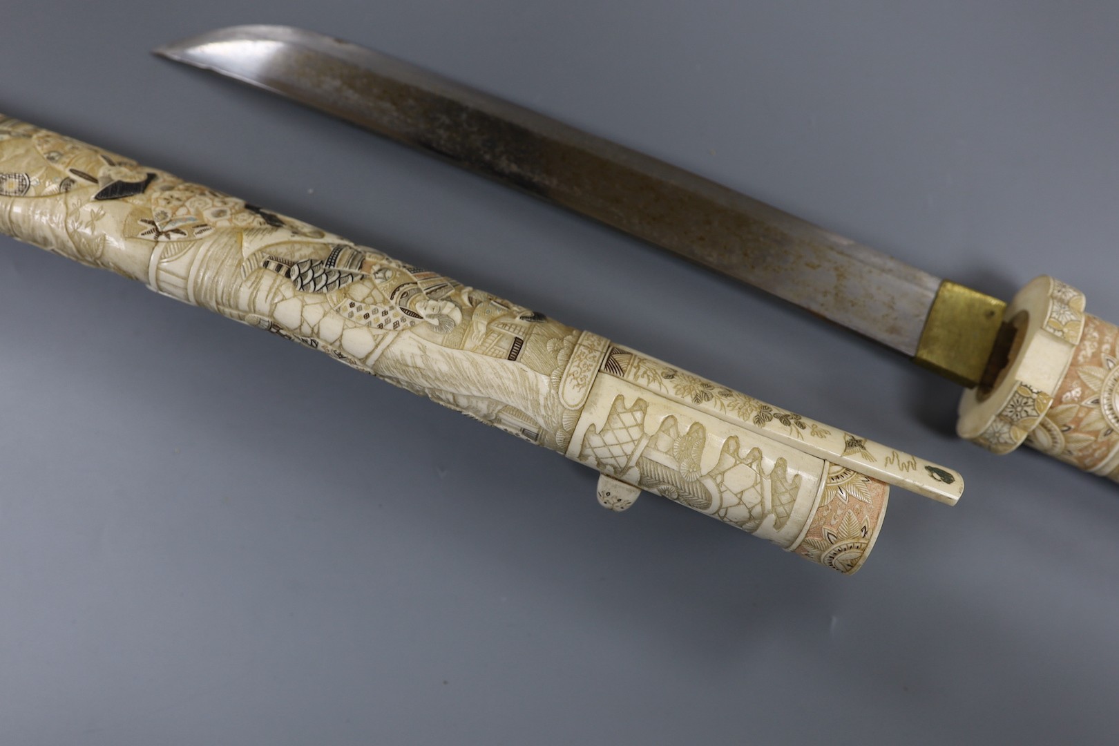 A Japanese carved and coloured ivory tanto, Meiji period, the hilt and scabbard carved to both sides with figures in ceremonial dress, the whole etched in black , green and red, the separate kodzuka with ivory blade and